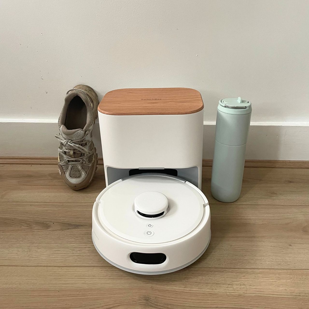 SwitchBot K11+ Robot Vacuum Cleaner with Mop, with a shoe on the left and a bottle on the right of it