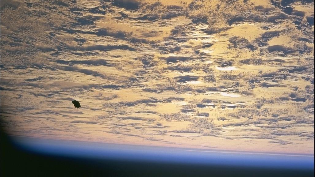 images captured from space show earth covered in clouds below and a small black object visible towards the left of the image.
