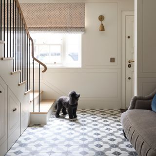 a dog in a hallway with floral patterned tiles looking at the door