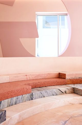 A pink-shaded flagship features brutalism-inspired, stone interiors like marble flooring along with porthole windows letting the light in.