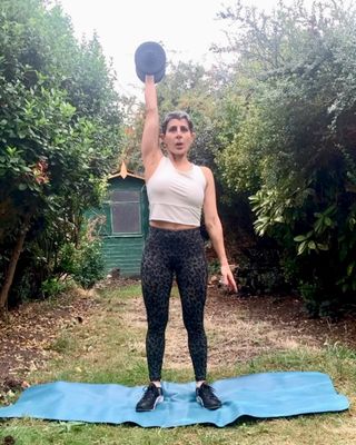 yanar alkayat woman short hair wearing white top dark leggings outside in garden holding weight overhead