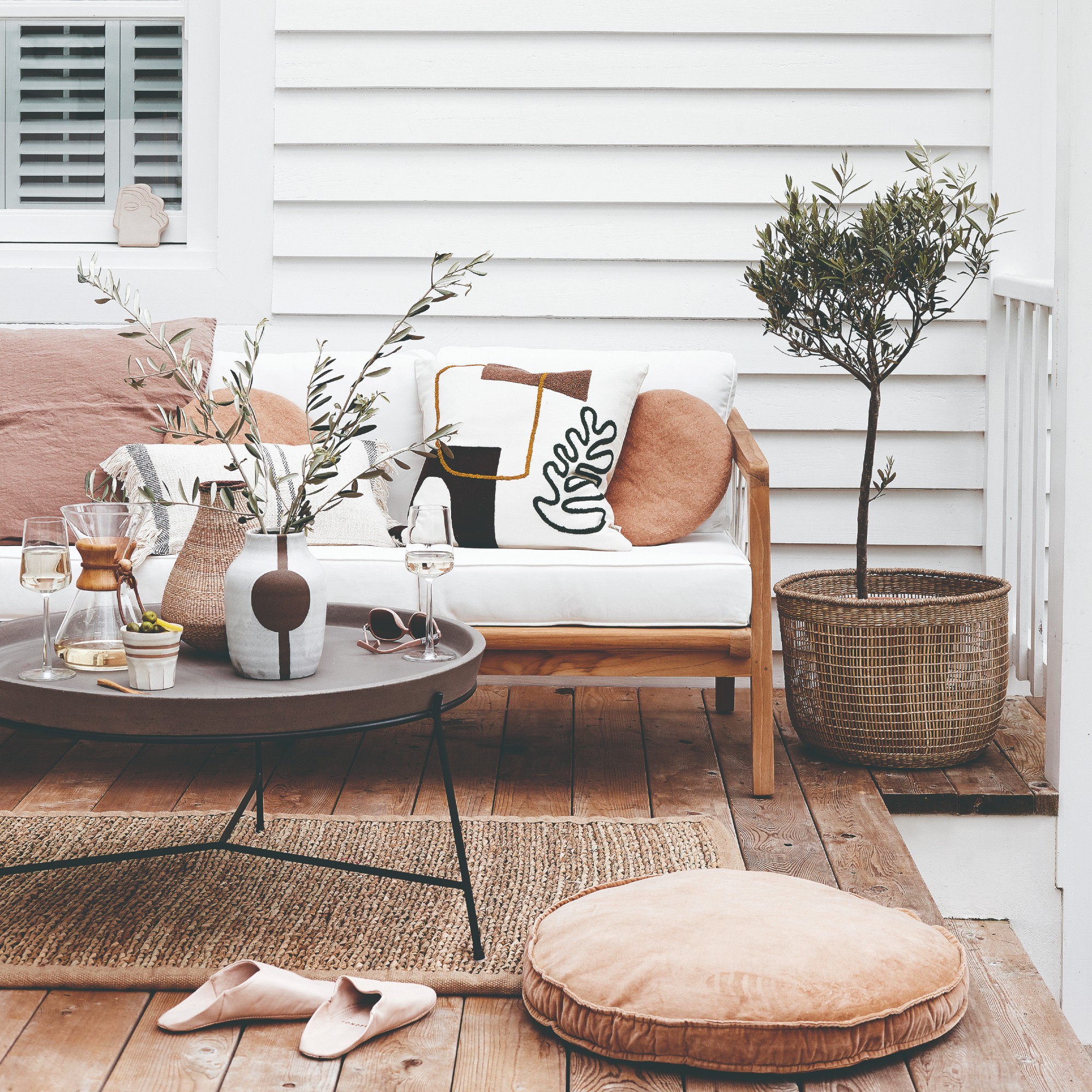 A deck with a wooden-frame outdoor sofa with white cushions and a round coffee table in front of it