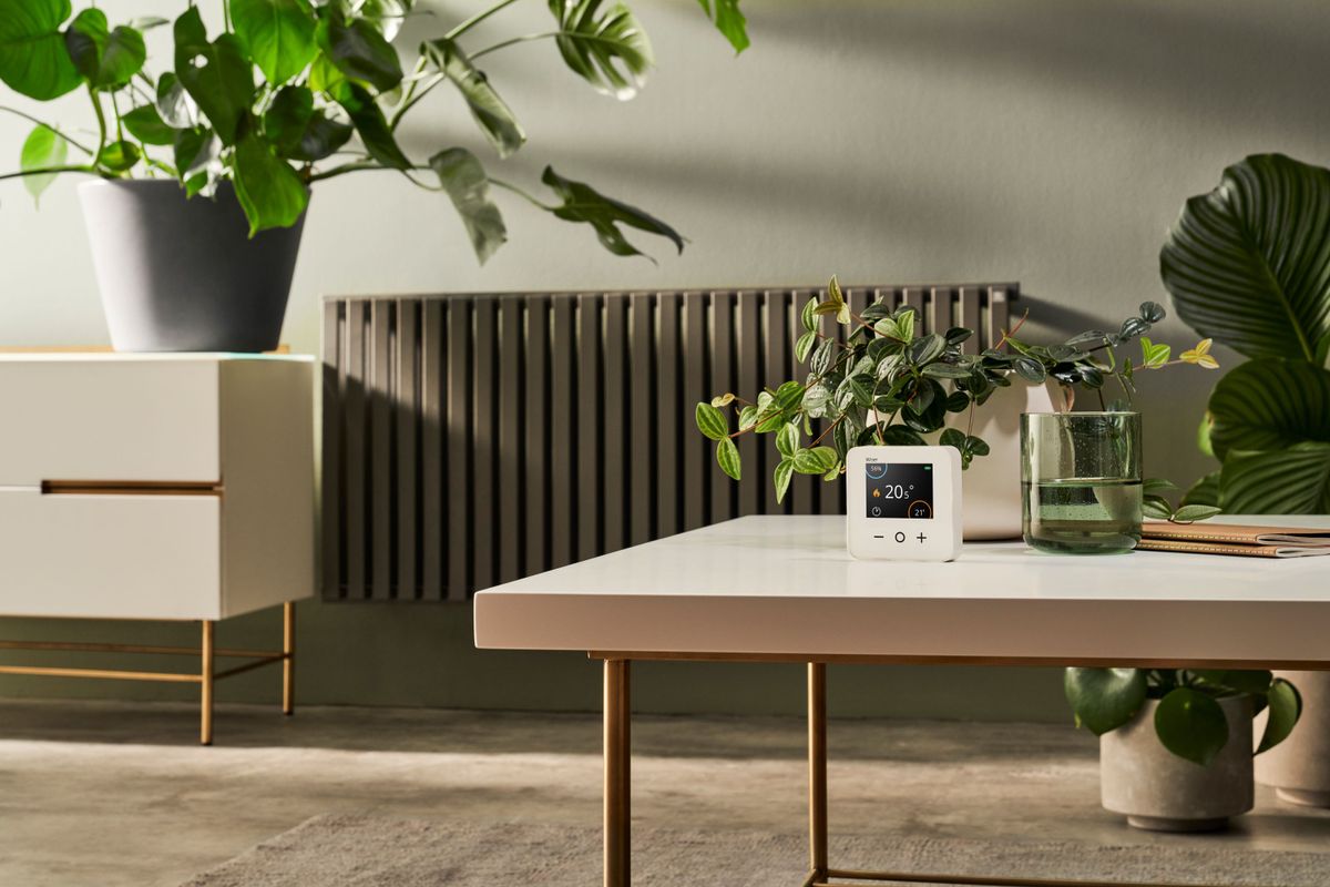 A Wiser smart thermostat sits on table in a room with a radiator behind it 