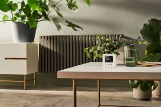 A Wiser smart thermostat sits on table in a room with a radiator behind it 