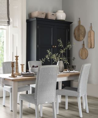 A grey dining room with light grey wicker chairs, wooden table and wooden chopping boards hanging on the wall
