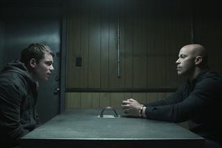 Gabriel Basso as Peter Sutherland and Berto Colon as Solomon talk over an interrogation table in the night agent