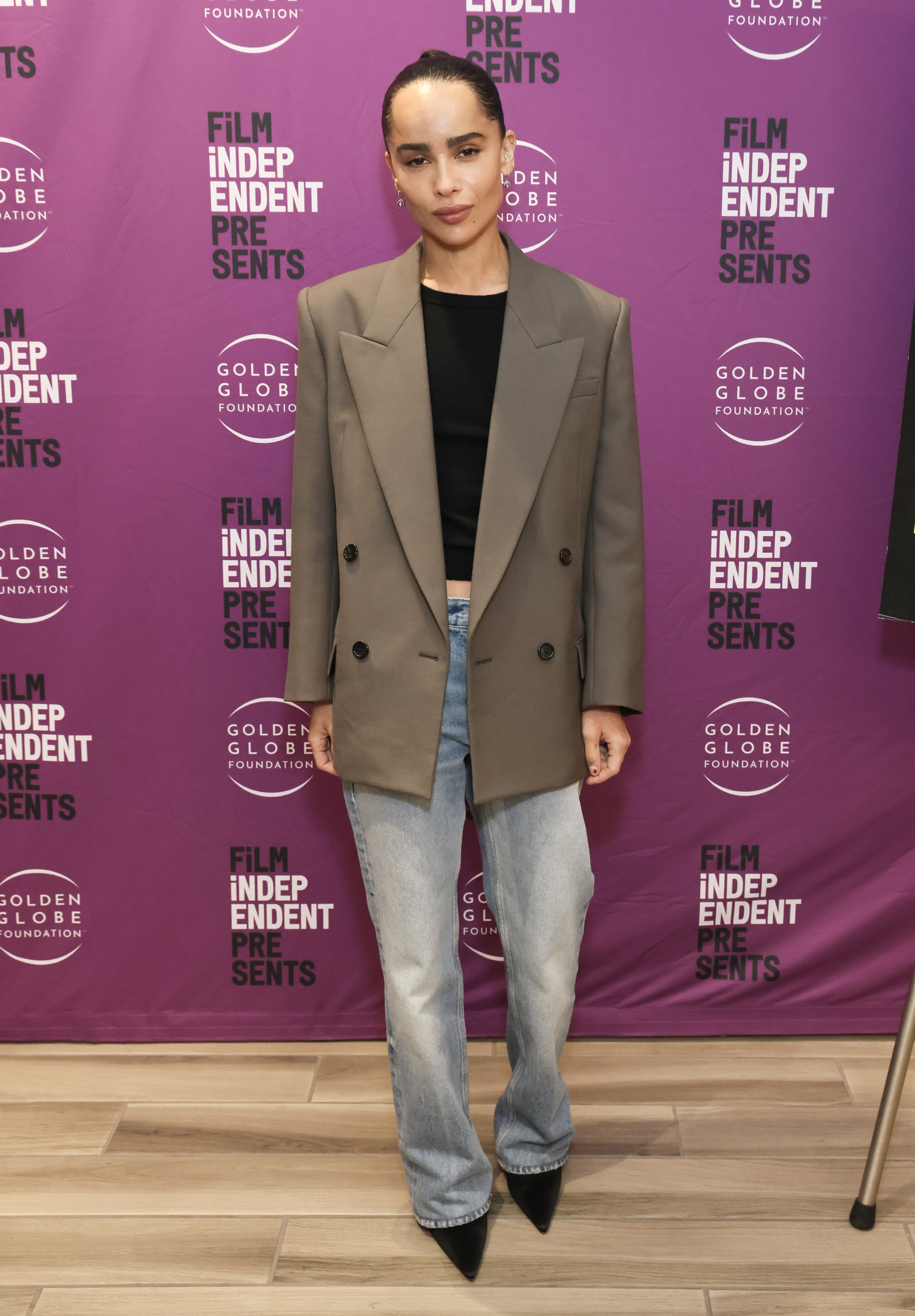 Zoe Kravitz wears a brown blazer, black T-shirt, baggy jeans, and black pumps.