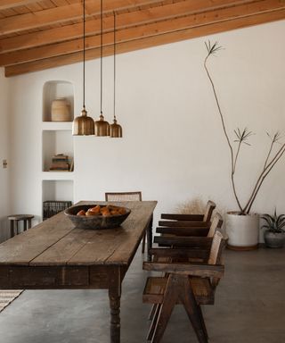 discovering your interior design style, rustic dining room with large wood table, chairs, concrete floor, beams, brass pendant lights, alcoves, plants