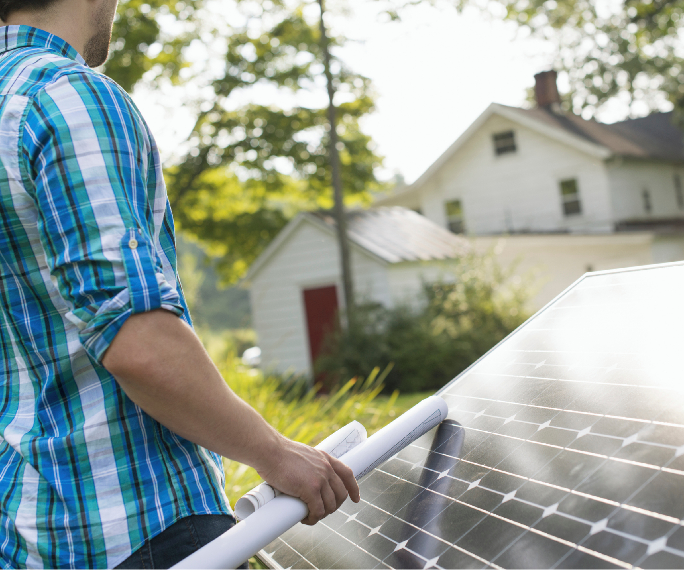 male holding rolled up paper drawings resting on solar panel with house in background