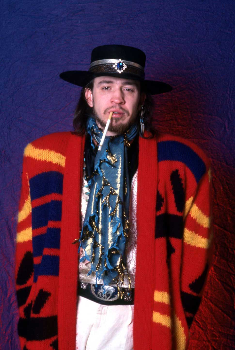 Steve Ray Vaughan backstage, wearing a poncho and smoking an unusually long cigarette