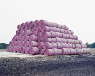 A large pile of hay balls stacked one on top of each other. There is a purple hue to it.