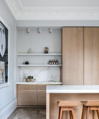A kitchen with light wood cabinets, white worktops and wooden bar stools