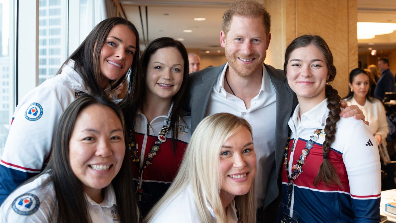 Prince Harry smiling and posing with five women wearing red, white and blue Team USA shirts at an Invictus Games event 