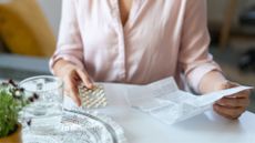 Woman's hands on a packet of HRT tablets and holding an instruction booklet at table at home