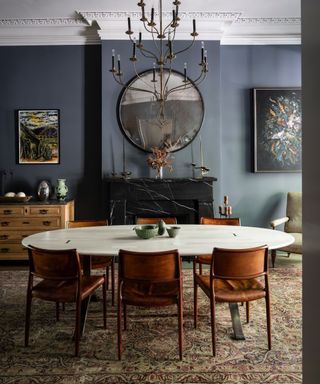ways with Down Pipe, blue dining room with oval table, tan dining chairs, vintage rug, sideboard, artwork, large chandelier, mirror