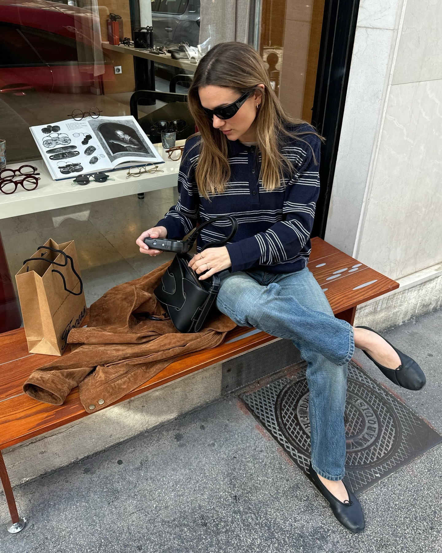 French woman wearing a travel outfit that includes a striped long-sleeve polo shirt, jeans, and black ballet flats