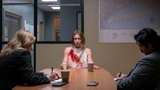 Police question Chloe in an interview room, she is looking upset and wearing a white dress which is covered in blood