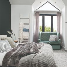A bedroom with a bay window with a green loveseat and a black feature wall
