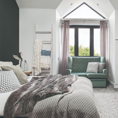 A bedroom with a bay window with a green loveseat and a black feature wall