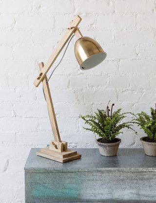 Luxe Loft Table Lamp with a wood base and arms with a brass shade, on top of a grey table next to small plants