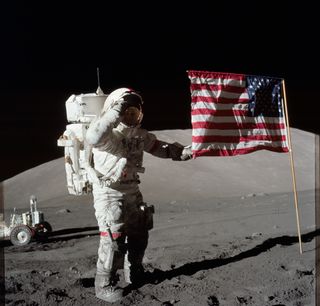 Eugene A. Cernan stands next to the United States flag on the lunar surface while saluting.