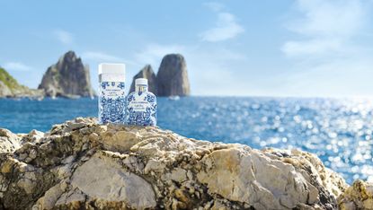 Two bottles of Dolce &amp; Gabbana Light Blue Summer Vibes perfume sitting on a rocky cliff overlooking the sea.