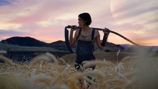 Kora stands in a field of wheat with a scythe over her shoulders in Rebel Moon Part 1