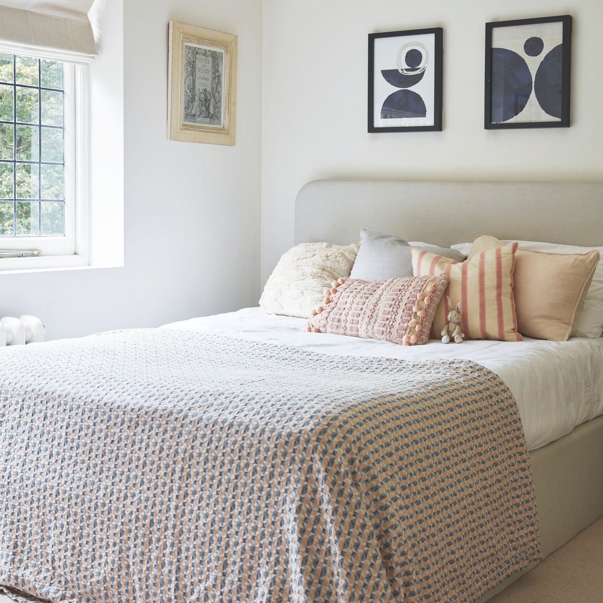 Neutral bedroom with cosy bed and pictures on the painted white walls around it