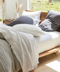 Black, white, and blue sheets on a bed against a window with a garden view. 