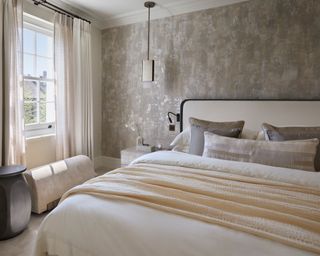 neutral bedroom with shimmer effect wallpaper, bed with cream headboard, pendant and cream curtains