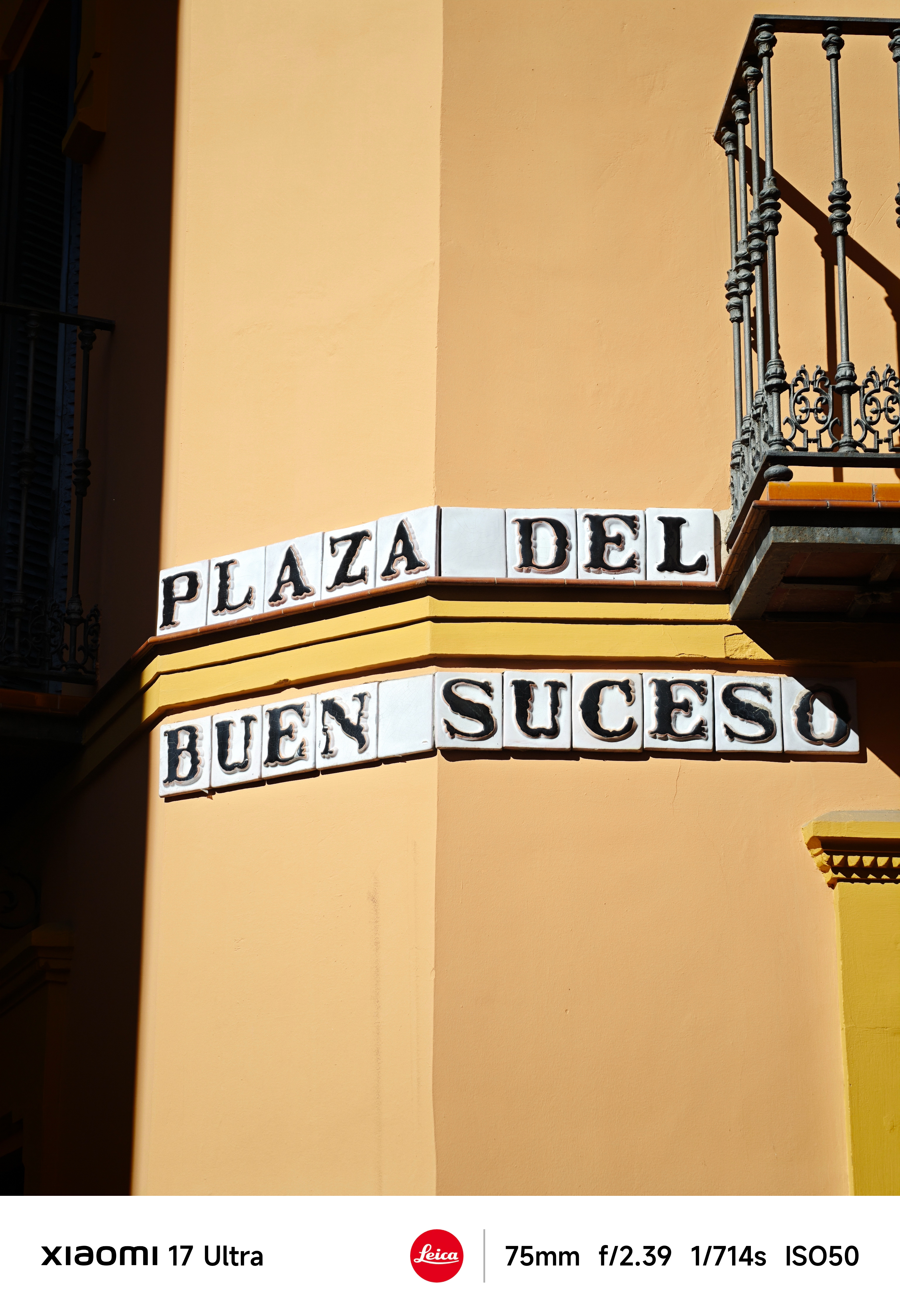Corner of a yellow building with ceramic street sign reading “Plaza del Buen Suceso” and wrought-iron balcony above.