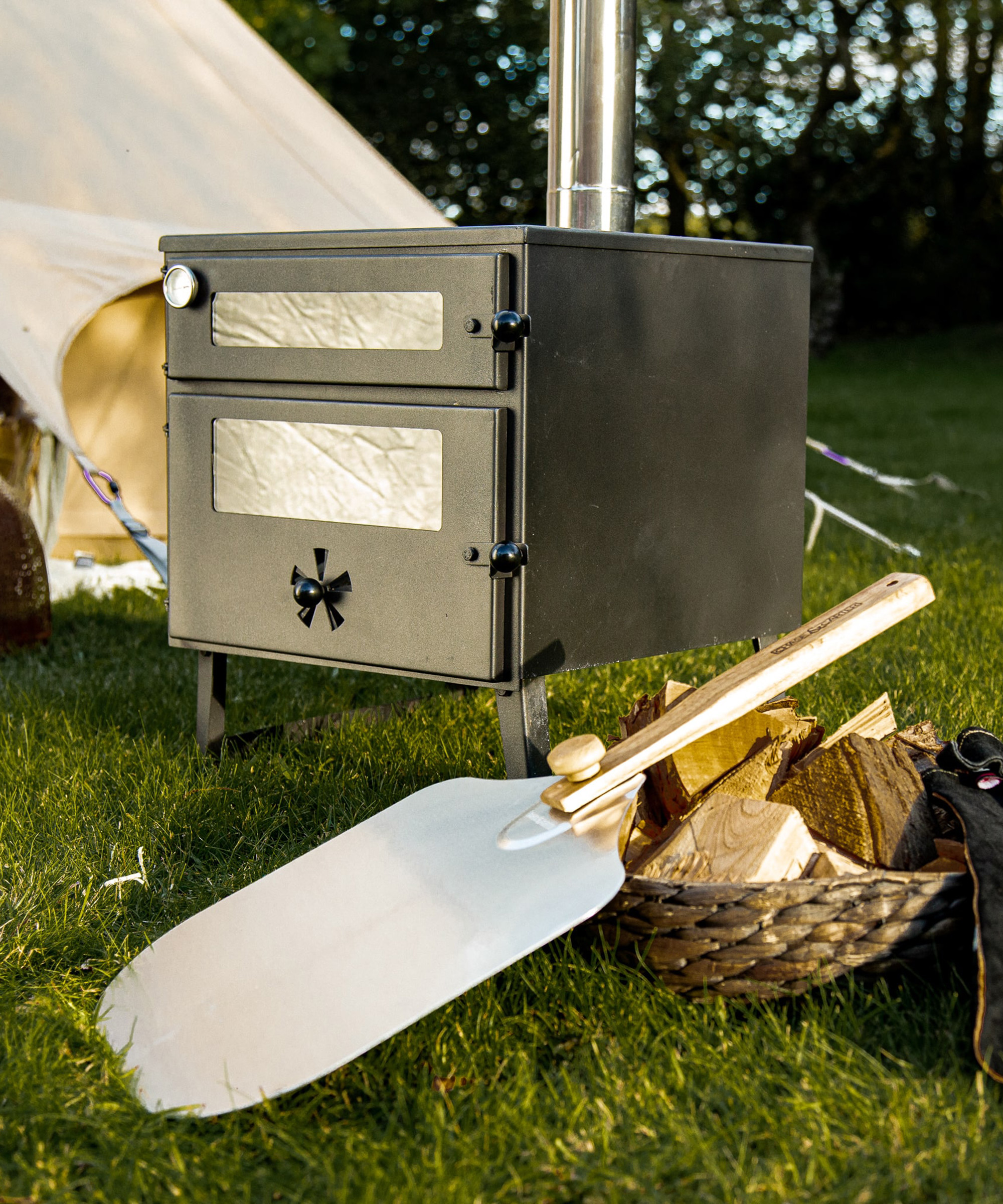 a wood burning stove next to a tent with a pizza stone