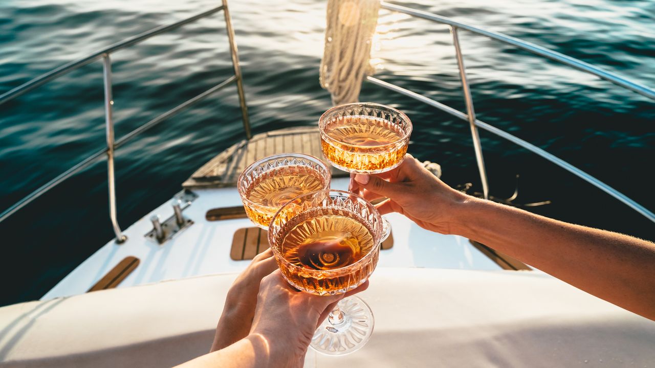 A champagne toast on a yacht, only the boat, water, hands and glasses showing.