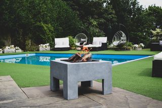 Chunky gray firepit in large back yard with in-ground pool and egg chairs