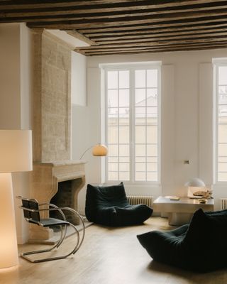 Living room with black chairs, a fireplace and large windows of the Le Marais apartment by Saba Ghorbanalinejad