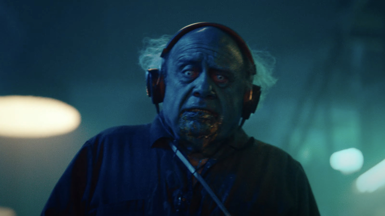 Danny DeVito como un conserje macabro con auriculares en Beetlejuice Beetlejuice