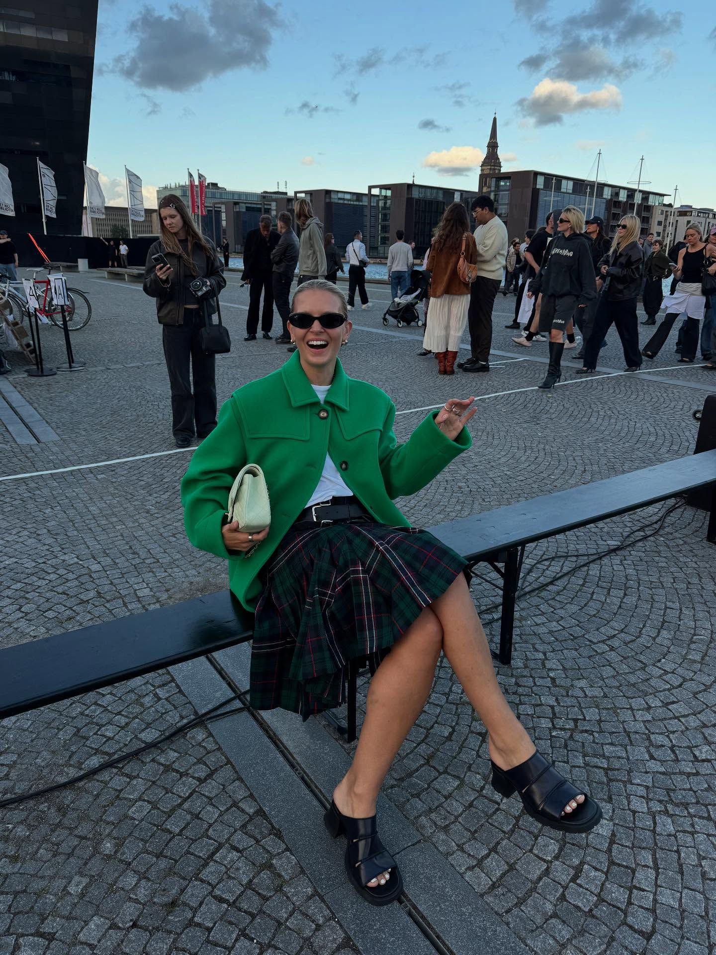 Hollie Mercedes Peters wears a green jacket, white tee, tartan kilt and black sandals during fashion week