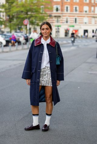 woman wearing barn jacket, white blouse, skirt, loafers, and socks