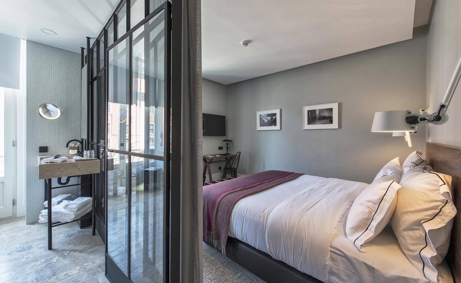 Interior view of the 1908 hotel room. A large bed is to the right and the bathroom to the left, which is divided by glass construction, separating it from the room itself.