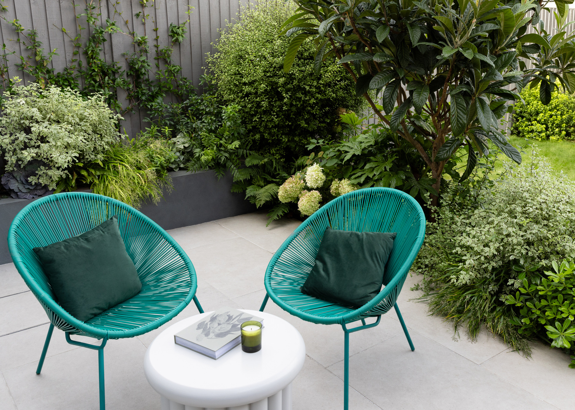 Two turquoise string chairs on a grey patio in a garden