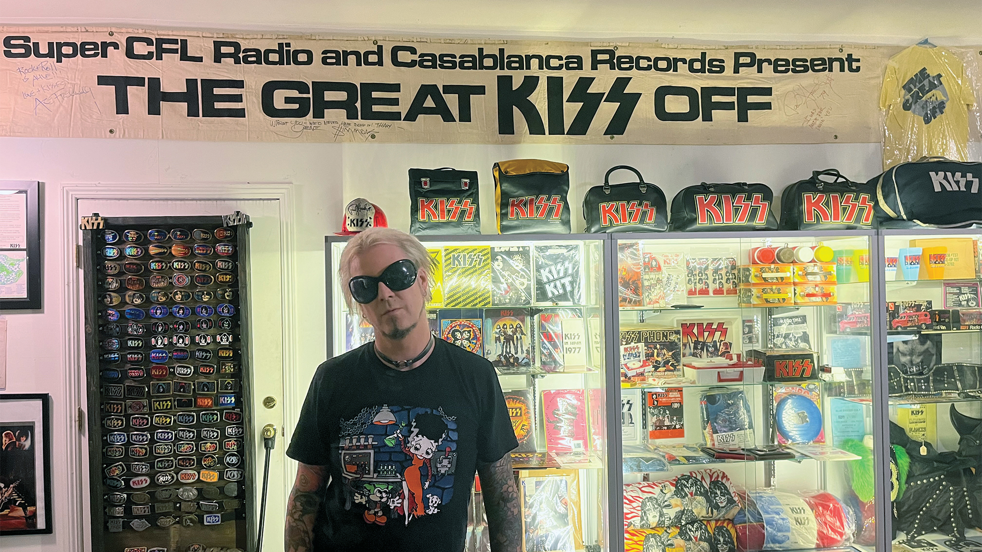 John 5 poses in his Knights in Satan's Service Museum of Kiss Memorabilia. This 1974 “Great Kiss Off” banner, from a promotion for the group’s debut album, held in a suburban Chicago mall, is among the rare one-offs in John’s collection. 