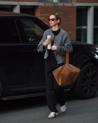 Anouk trug eine graue Kurzjacke, ein schwarzes Top, eine schwarze Hose, weiße Adidas Sambas und eine braune Wildledertasche.