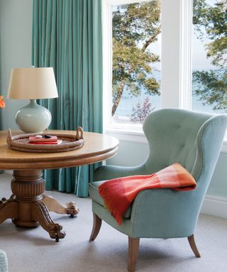 A living room with a blue armchair, wooden table and outdoor lake view