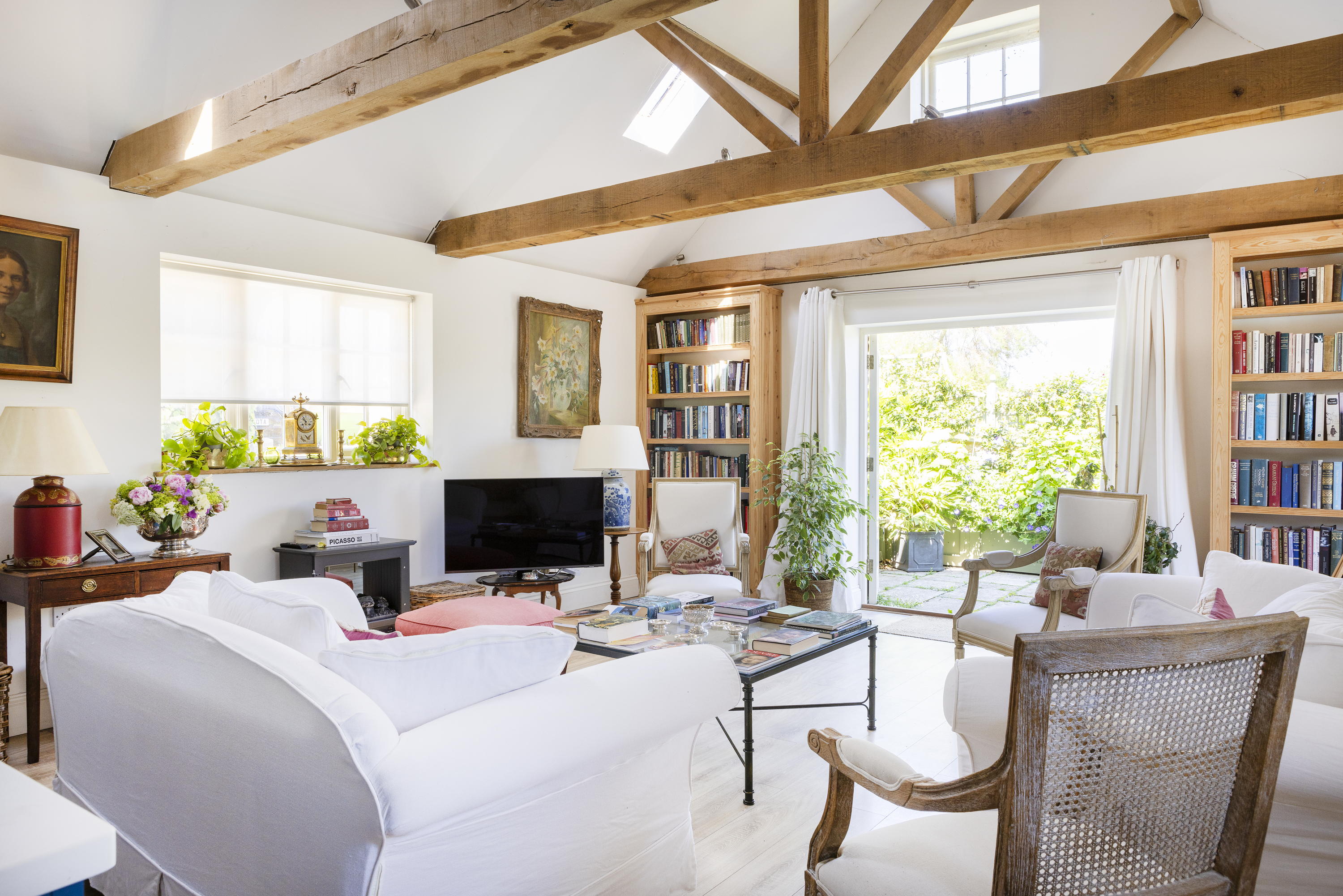 Mount Farm's living room — a well-lit room with exposed wooden beams, a television and white sofas and chairs, as well as wooden bookshelves