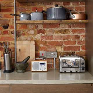kitchen area with brick wall and toaster and pots and pans on floating shelves