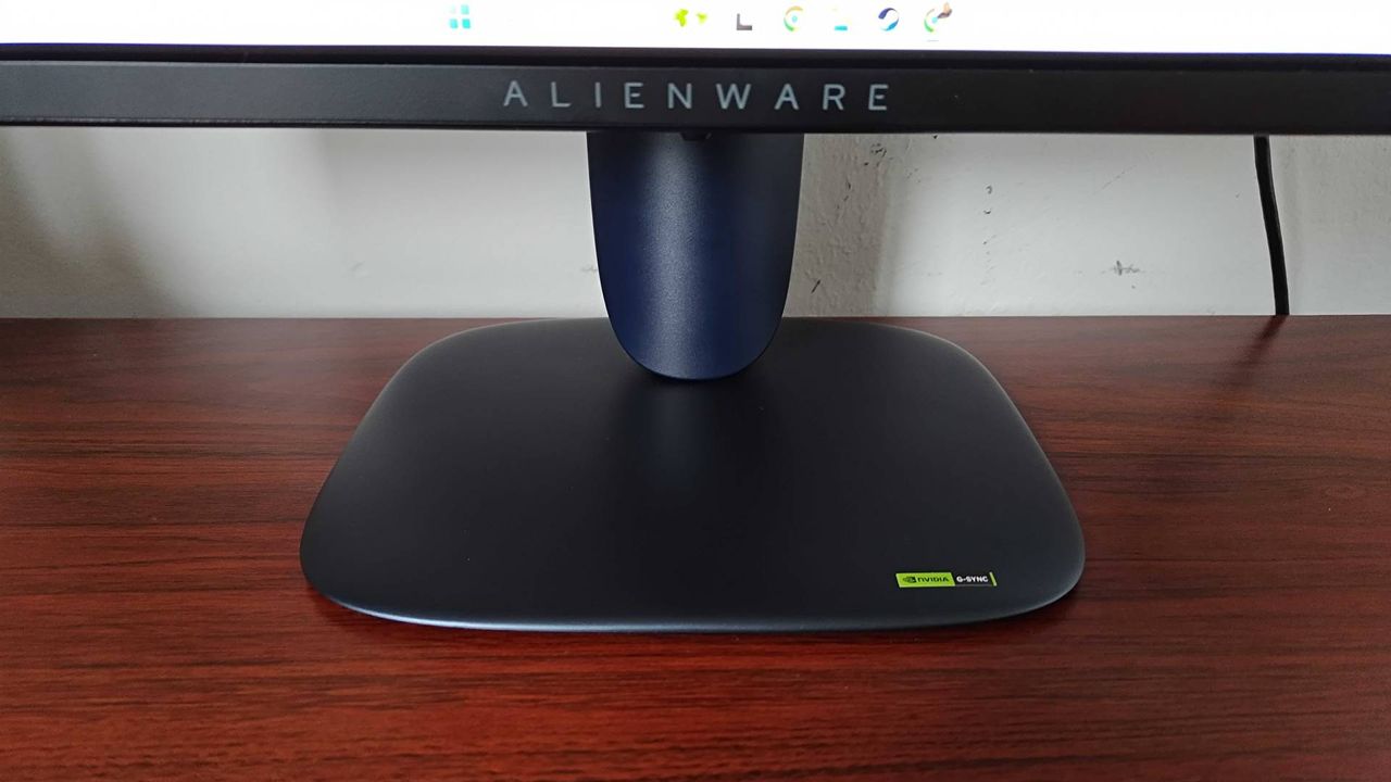 Close up of Alienware AW2725Q gaming monitor stand sitting on woodgrain desk.