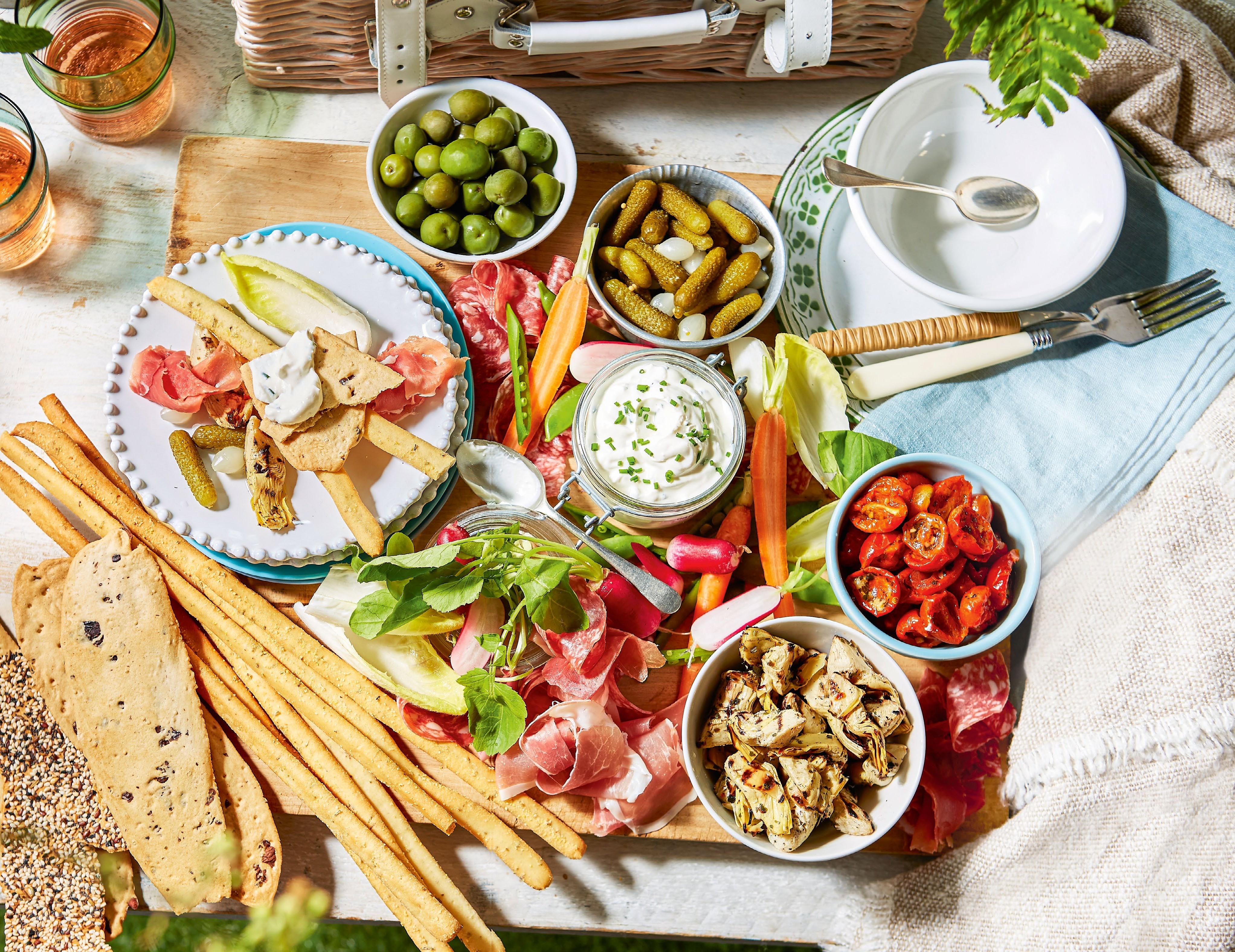 A beautifully arranged antipasti platter featuring cured meats, olives, pickles, fresh vegetables, and dips, perfect for a posh picnic.