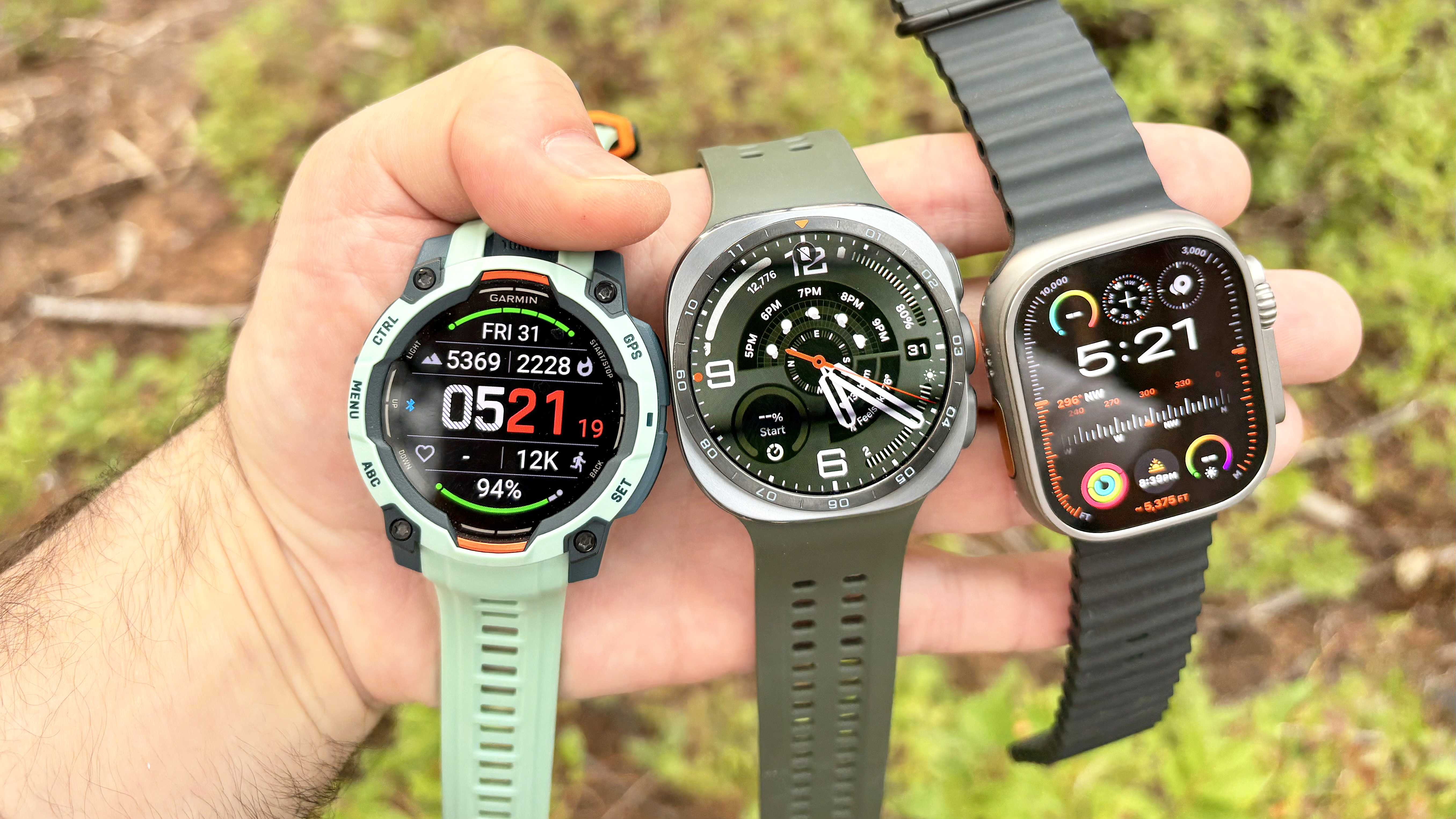 Close-up of the Samsung Galaxy Watch Ultra 2, Apple Watch Ultra 3 and Garmin Instinct 3 in nature