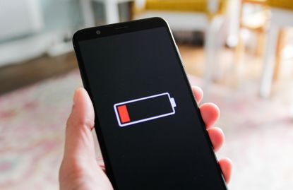 A hand holds a smart phone with a low battery sign.