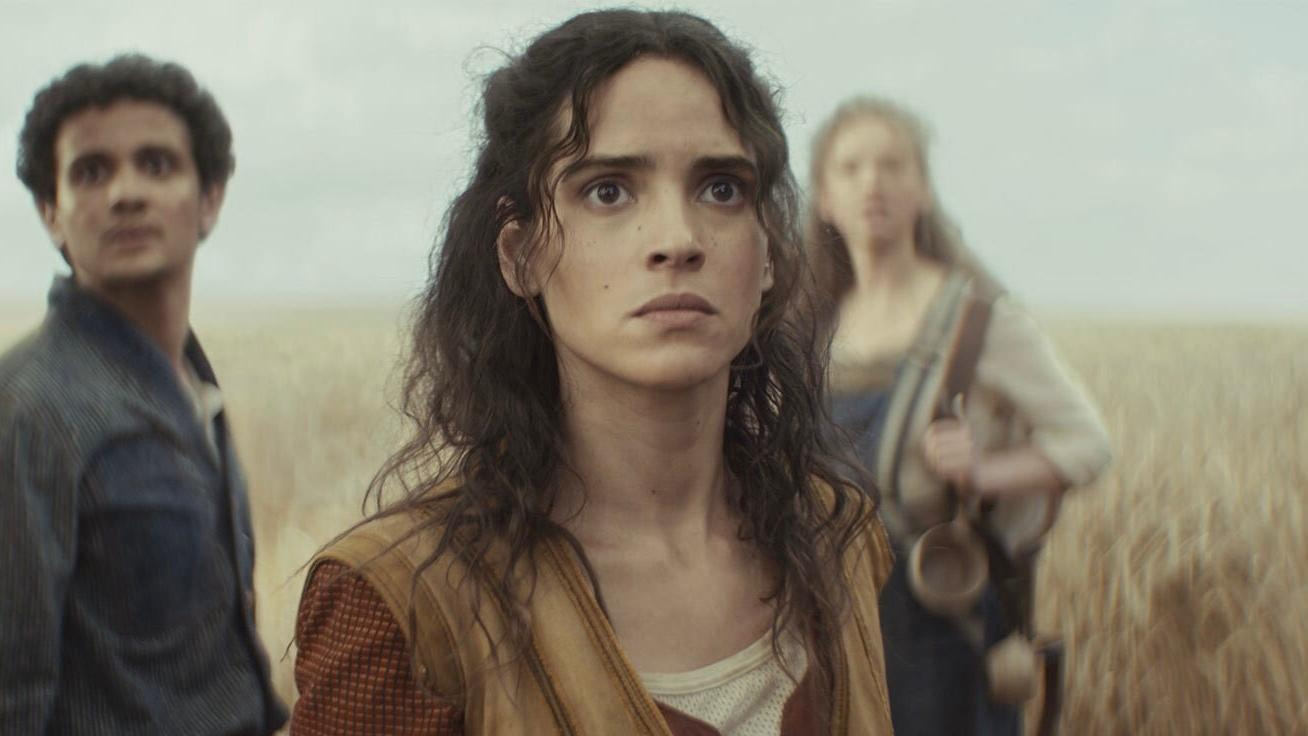 Still from the Star Wars TV show, Andor. Three people are standing in a field of grain. They are looking extremely worried.